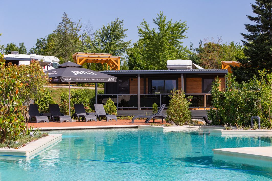The pool area at Plitvice Holiday Resort, surrounded by modern cabins, lounge chairs, and umbrellas.
